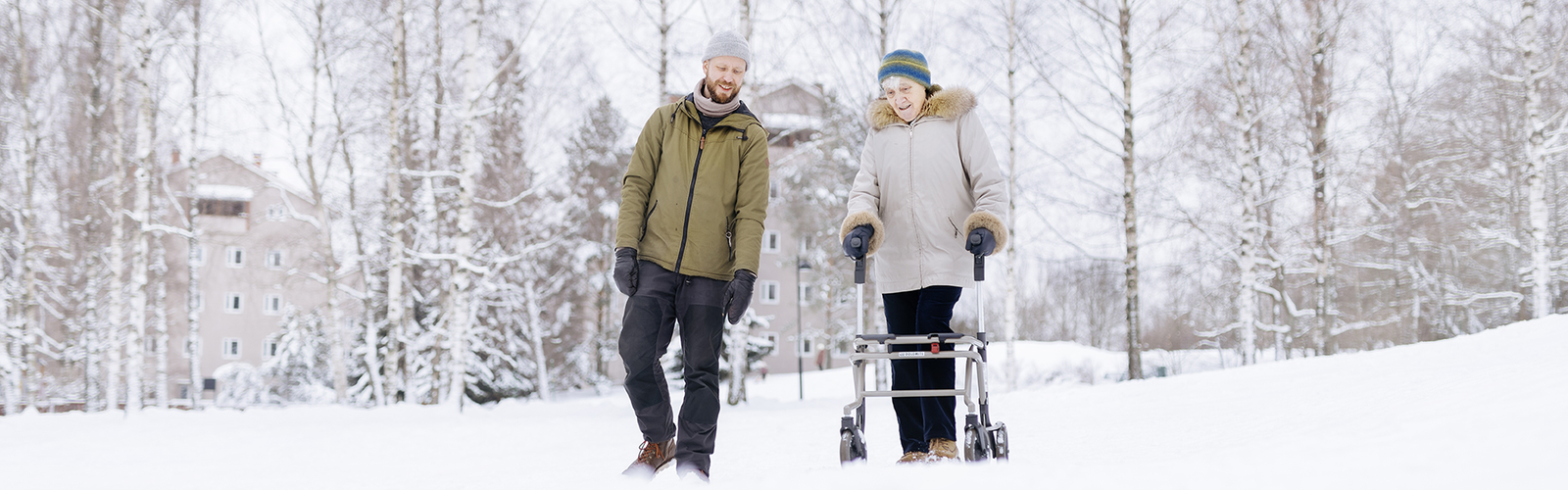 Kaksi henkilöä kävelee yhdessä lumisessa maisemassa ja juttelee.