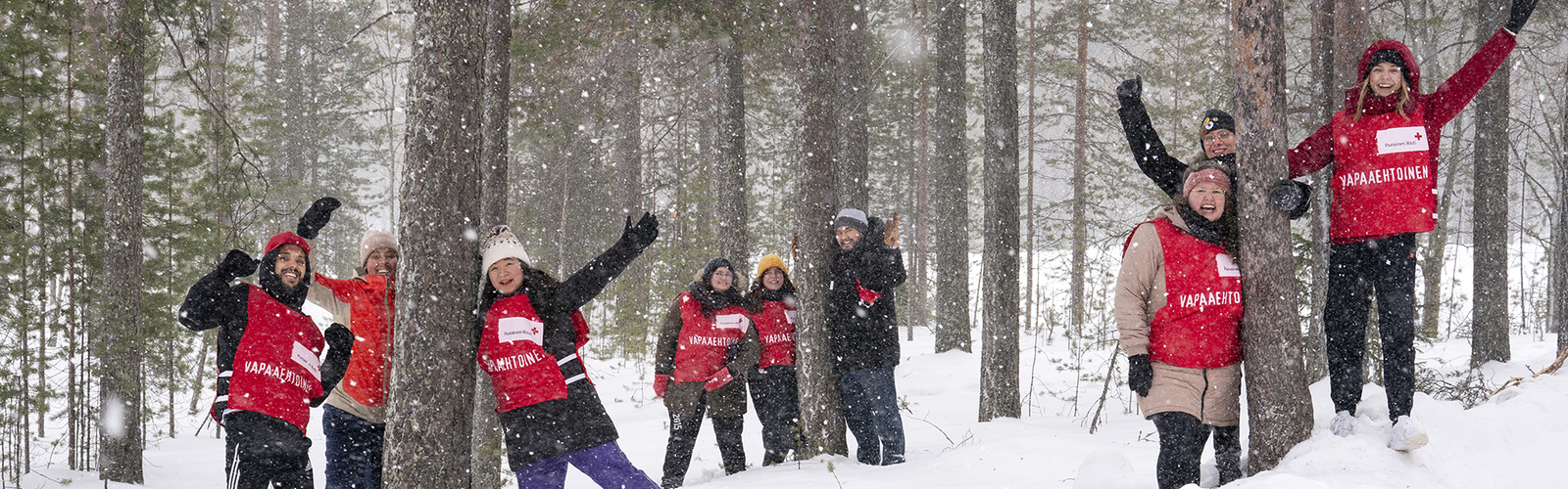 Ryhmä vapaaehtoisia leikkii lumella metsässä ja hymyilee kameralle.