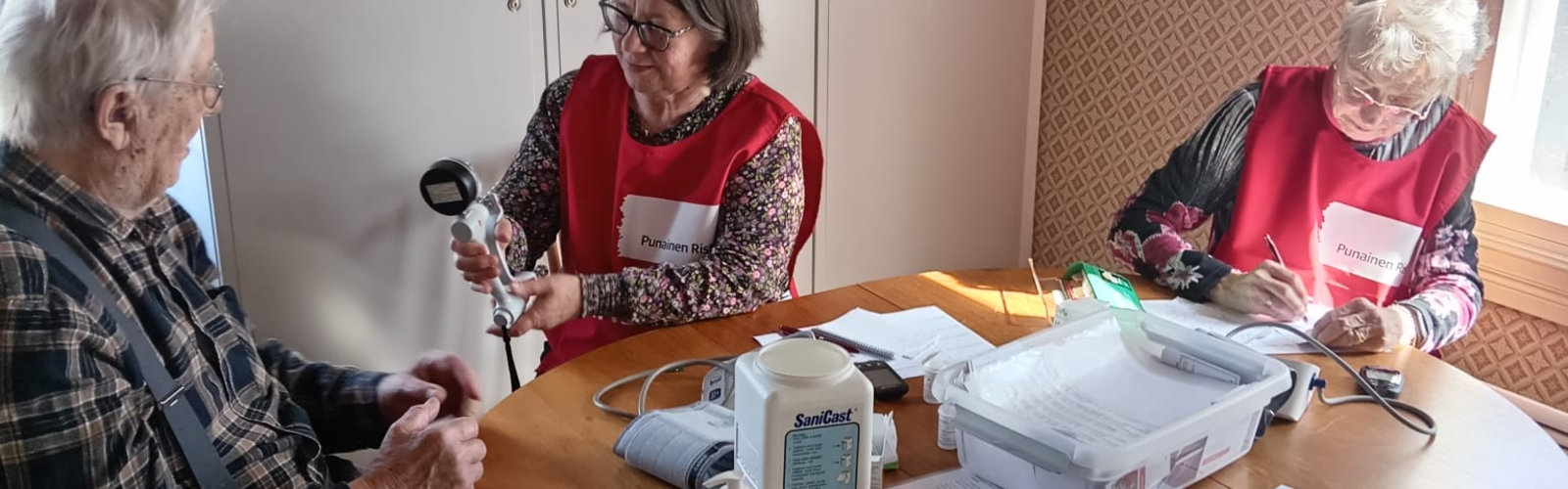 Kaksi terveyspisteen ammattilaista työssään. Asiakas mittauksissa.