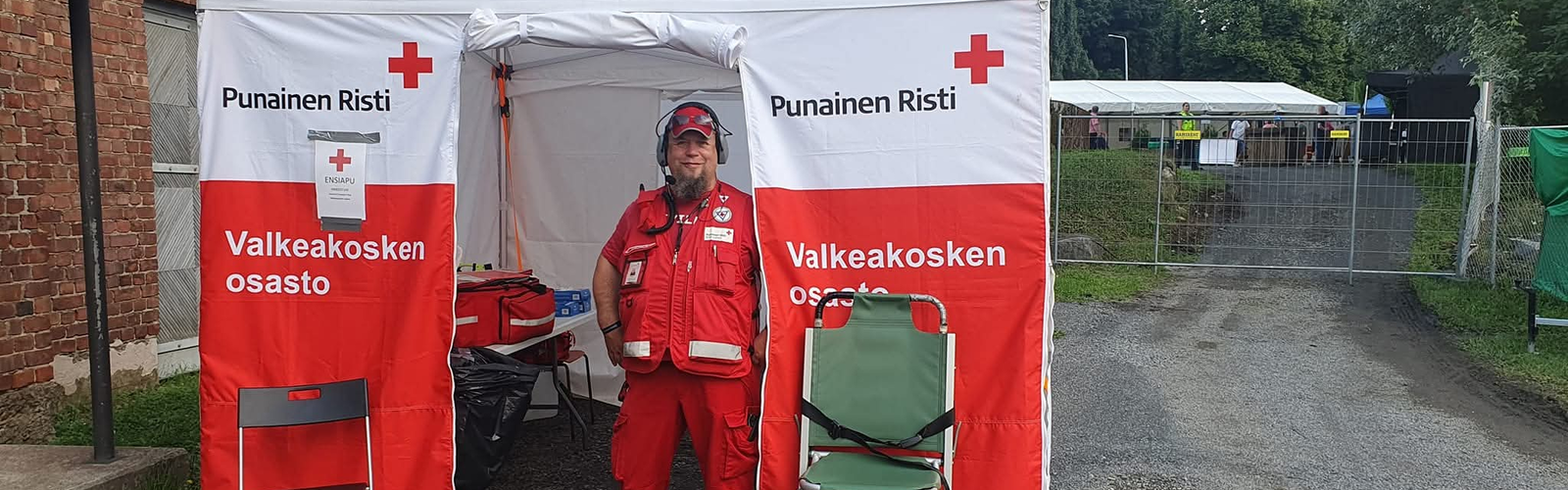 Ensiapupäivystäjä seisoo SPR:n teltan oviaukossa ja hymyilee.