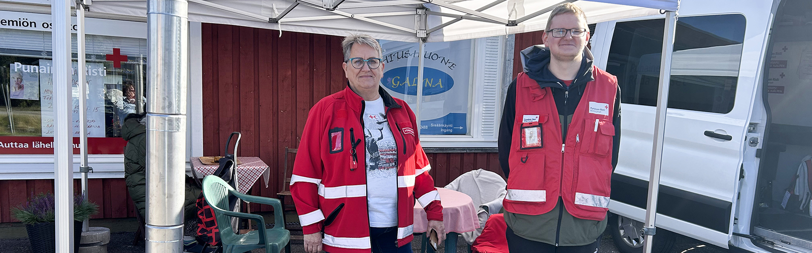 Två personer i rödakorsklder utanför en röd byggnad